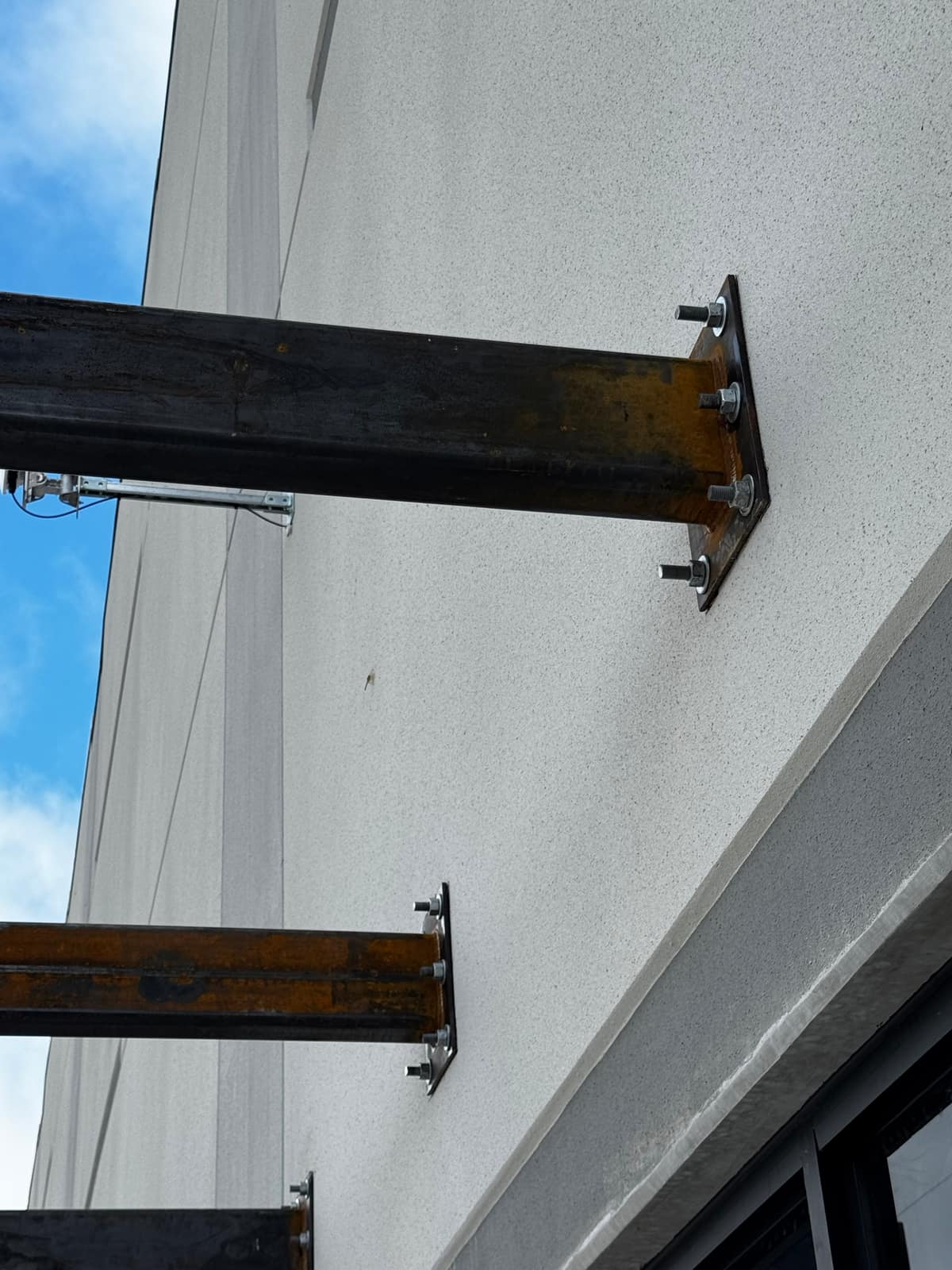Close view of two steel cantilever arms bolted to the precast wall through end plates and anchor bolts