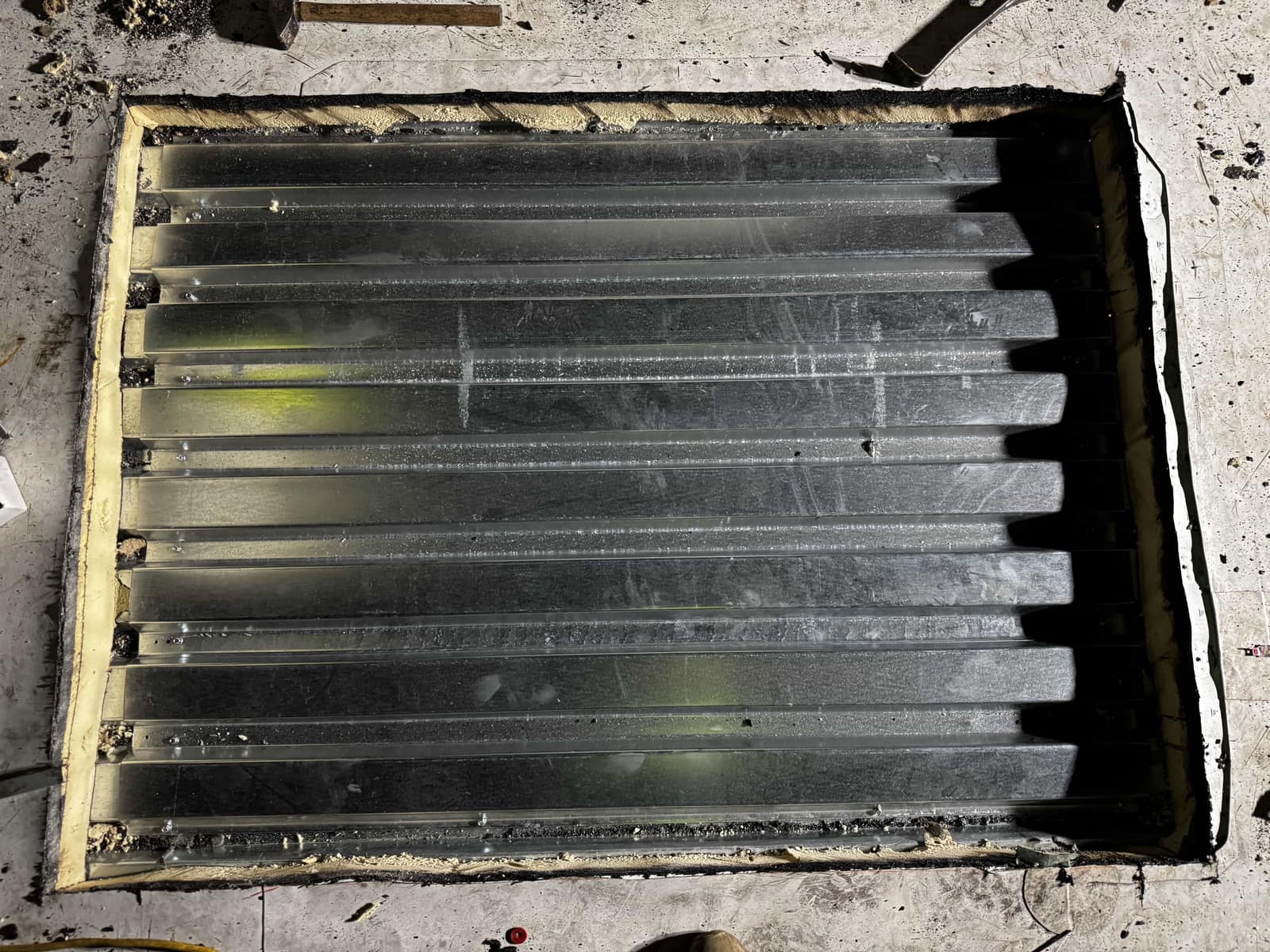 Overhead view of a section of corrugated metal deck fitted into a roof opening, its perimeter sealed, with insulation visible along one edge