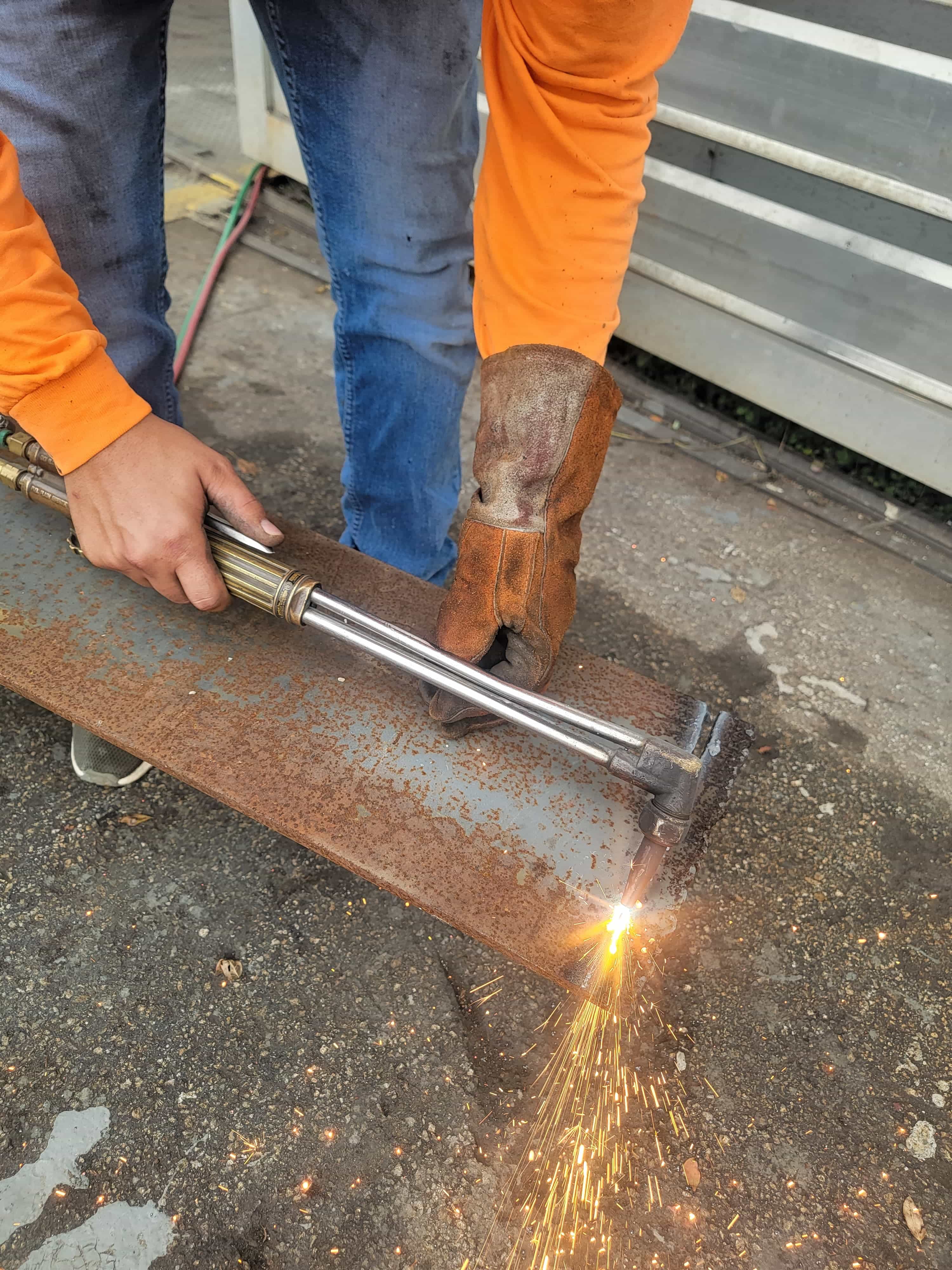 Oxy-fuel torch cutting a steel plate on site, sparks streaming onto the ground